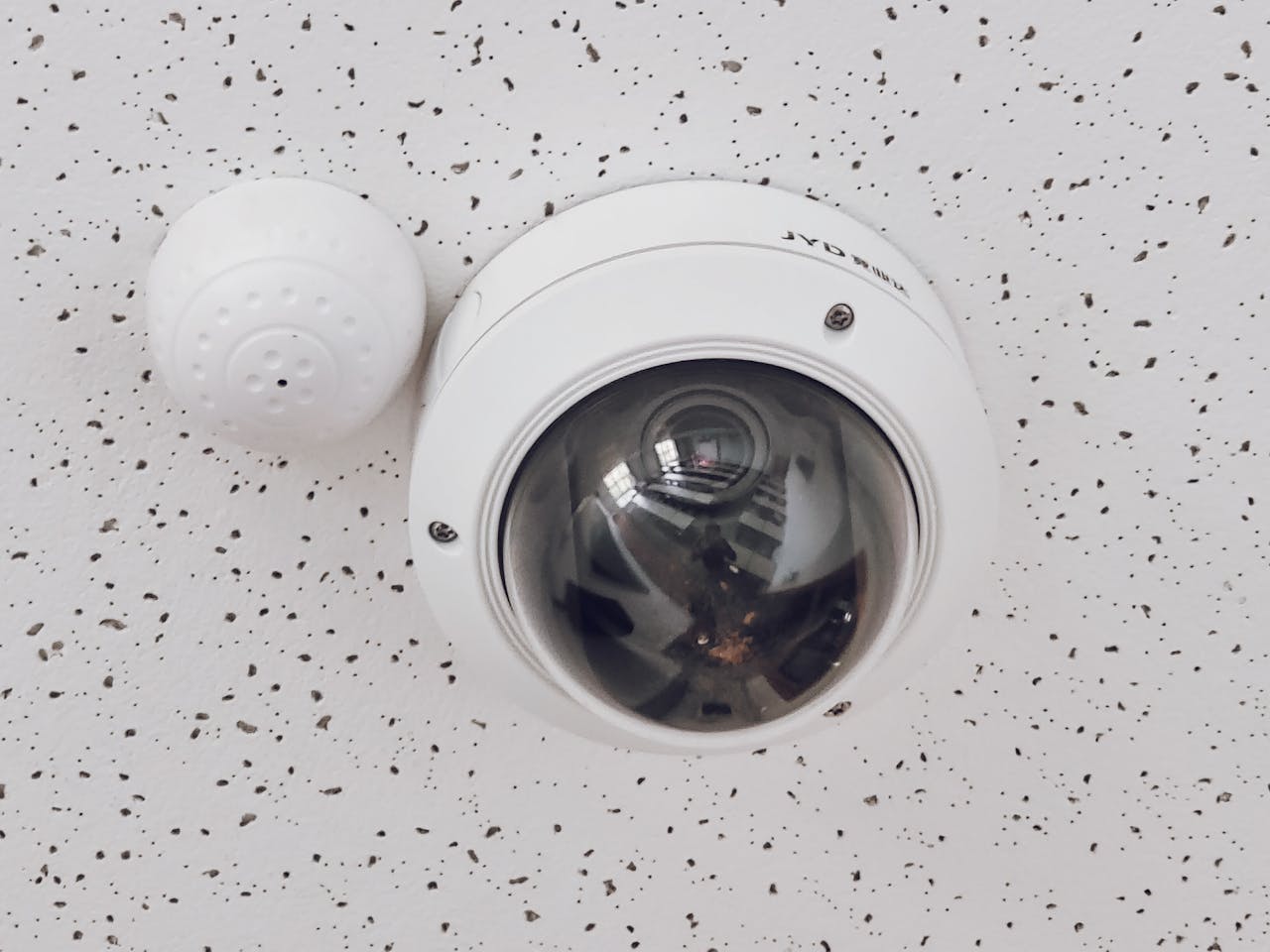 About Close-up of a round dome surveillance camera installed on a speckled ceiling for security monitoring.